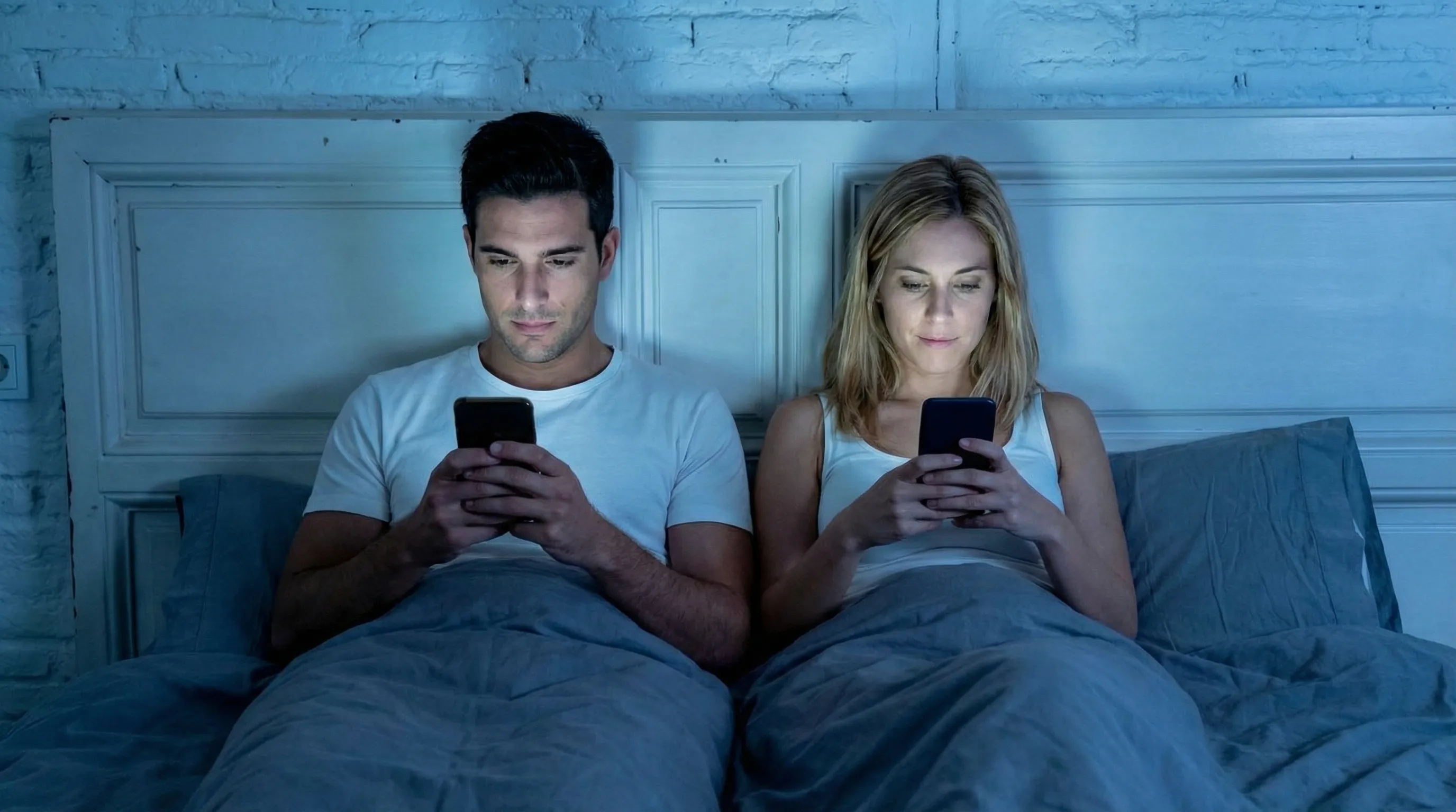 Couple using smartphones in bed at night showing digital addiction and disconnection from each other