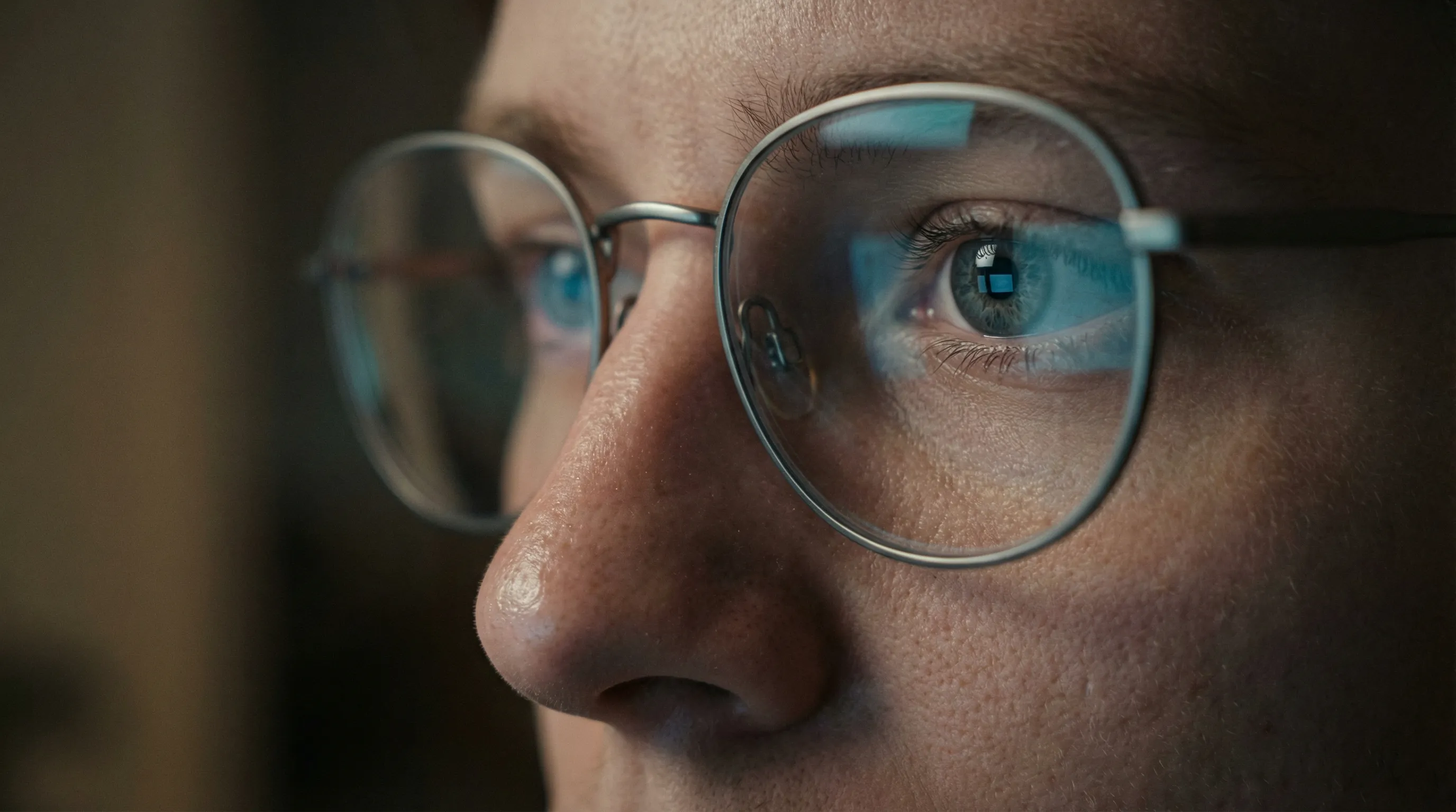 Close-up of person wearing glasses with blue light screen reflection showing digital eye strain from computer use